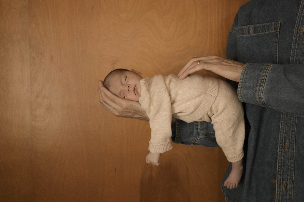 Paul holding newborn, editorial-style pose in a warm, wood-paneled room.