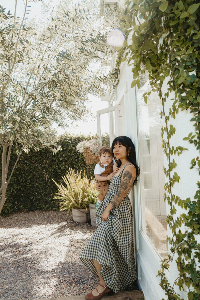 Mother cuddling toddler in a soft cotton dress during a cottagecore-inspired greenhouse motherhood session.