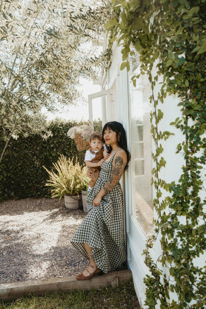 Mother cuddling toddler in a soft cotton dress during a cottagecore-inspired greenhouse motherhood session.