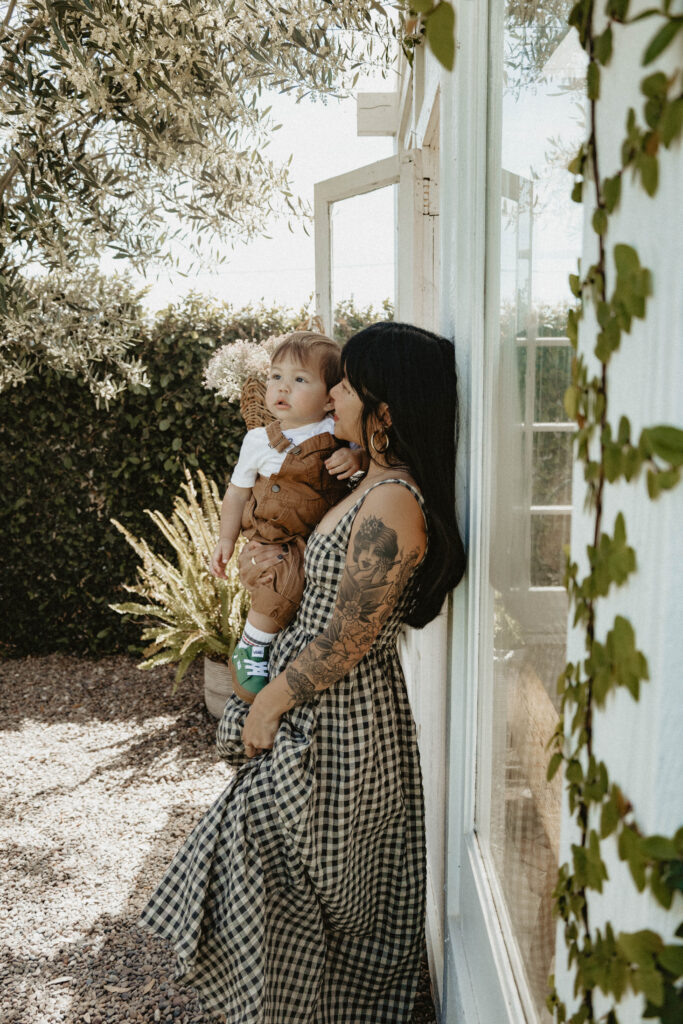 Mother cuddling toddler in a soft cotton dress during a cottagecore-inspired greenhouse motherhood session.