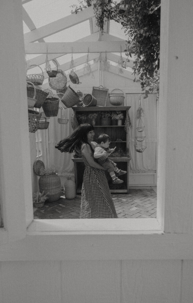 Mother cuddling toddler in a soft cotton dress during a cottagecore-inspired greenhouse motherhood session.