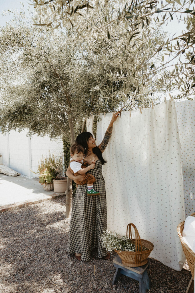 Mother cuddling toddler in a soft cotton dress during a cottagecore-inspired greenhouse motherhood session.