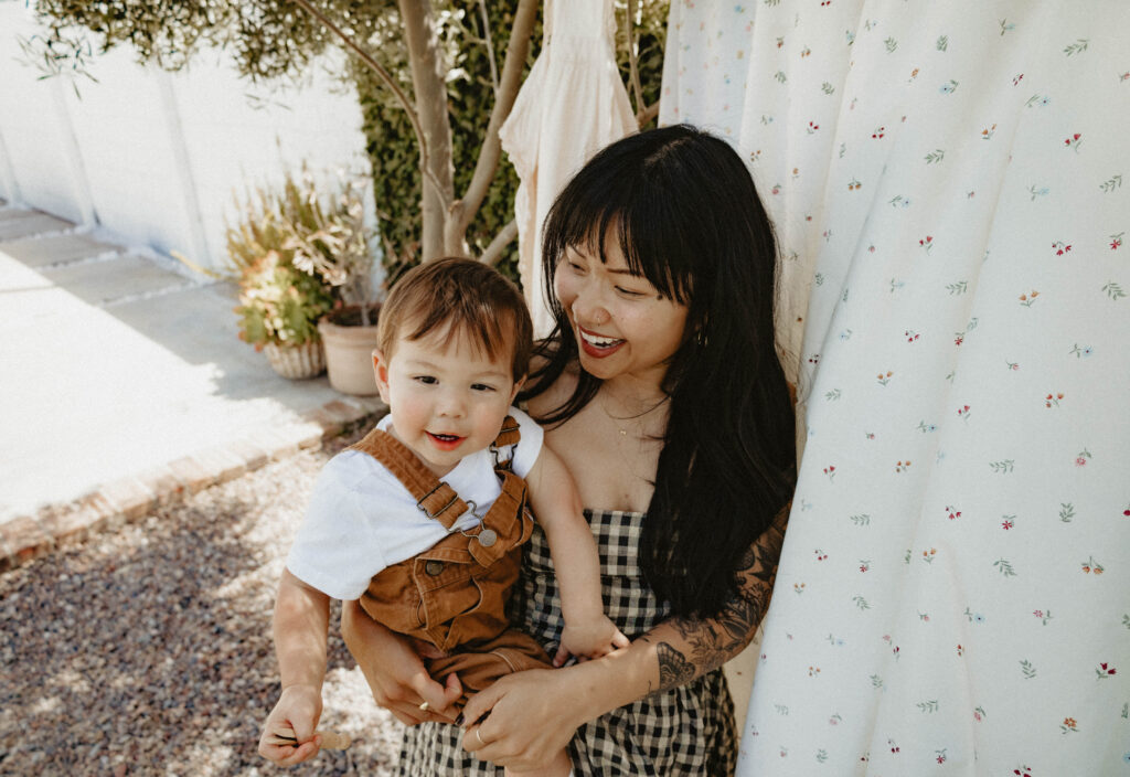 Mother cuddling toddler in a soft cotton dress during a cottagecore-inspired greenhouse motherhood session.