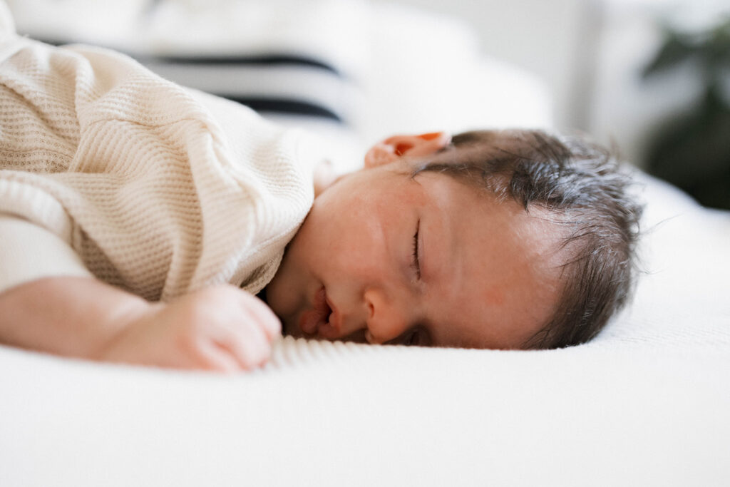 Newborn Rowan peacefully sleeps in a neutral clothes during an in-home family session, photographed in the space where he was born.