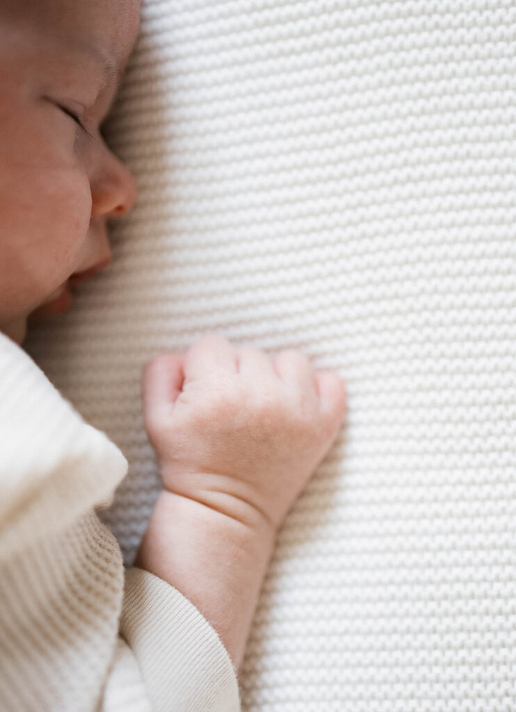 Newborn Rowan peacefully sleeps in a neutral clothes during an in-home family session, photographed in the space where he was born.