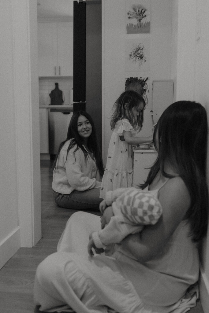 Playful moment during the Robbins’ in-home newborn family session, with older siblings dancing around while mom cuddles baby Rowan.