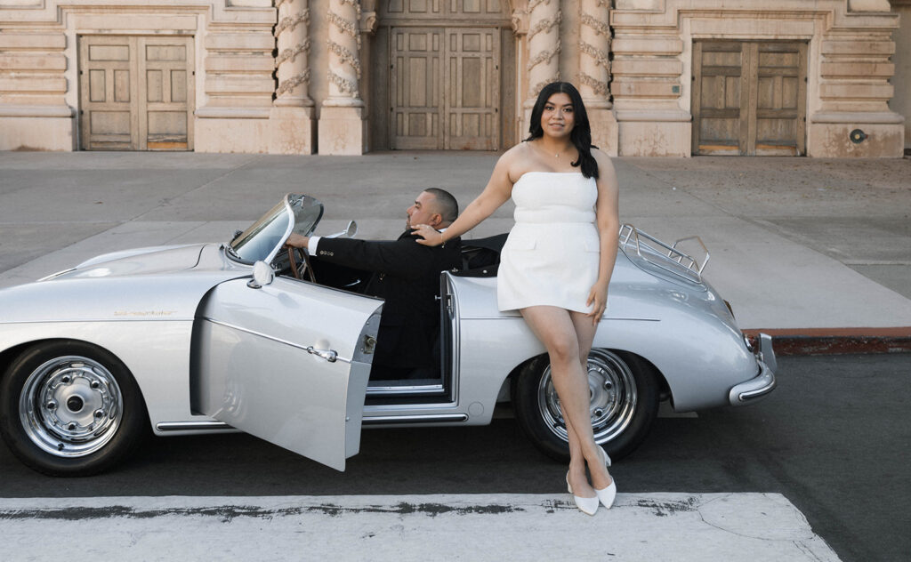 Sabrina and Azor posing in front of a classic vintage car from SD Vintage Rides at Balboa Park, exuding formal glamour.