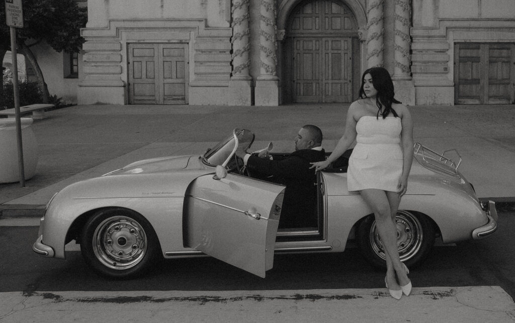 Sabrina and Azor posing in front of a classic vintage car from SD Vintage Rides at Balboa Park, exuding formal glamour.
