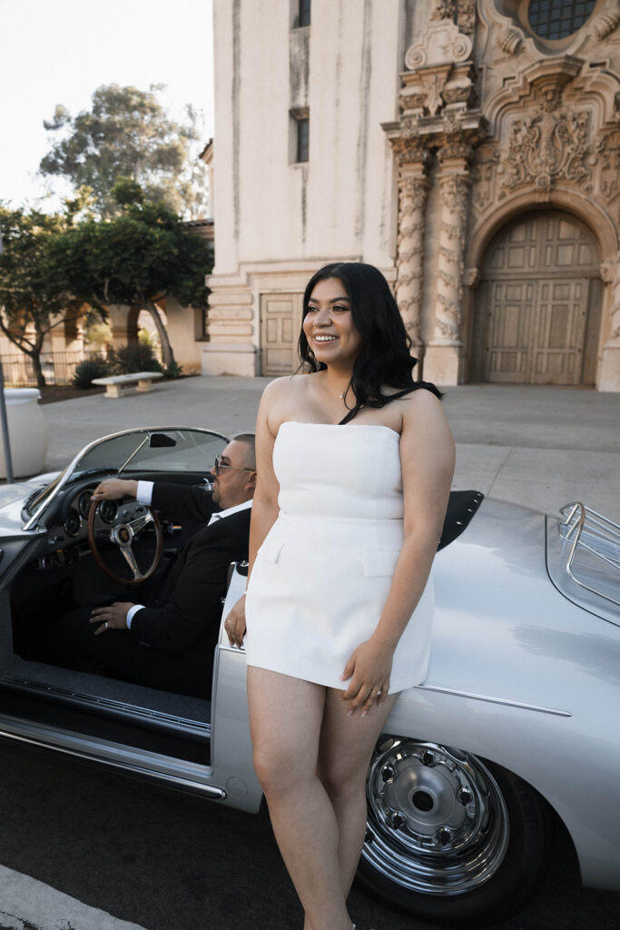 Sabrina and Azor posing in front of a classic vintage car from SD Vintage Rides at Balboa Park, exuding formal glamour.
