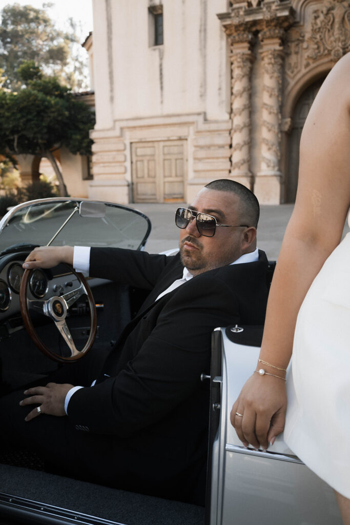 Sabrina and Azor posing in front of a classic vintage car from SD Vintage Rides at Balboa Park, exuding formal glamour.
