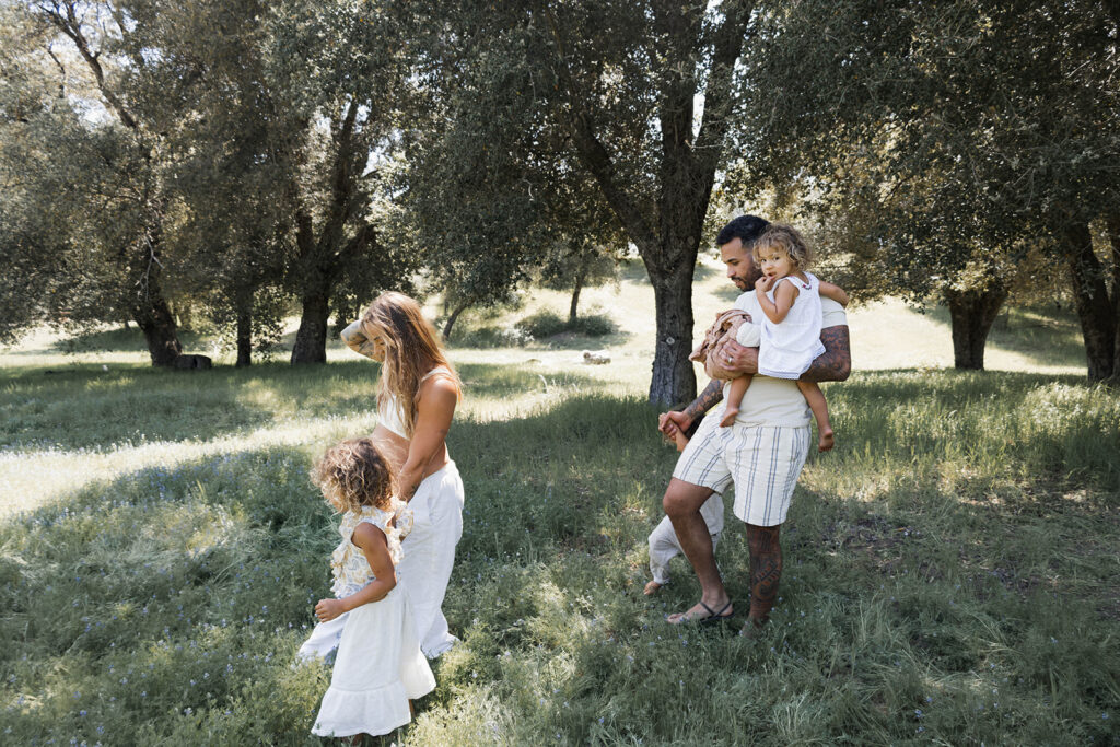 Family walking through a grassy field in a San Diego park during a maternity session, with pregnant mother holding hands with daughter and father carrying another child