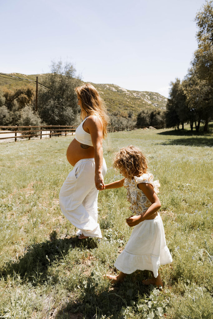 expecting mother walking hand in hand with oldest daughter in field of grass