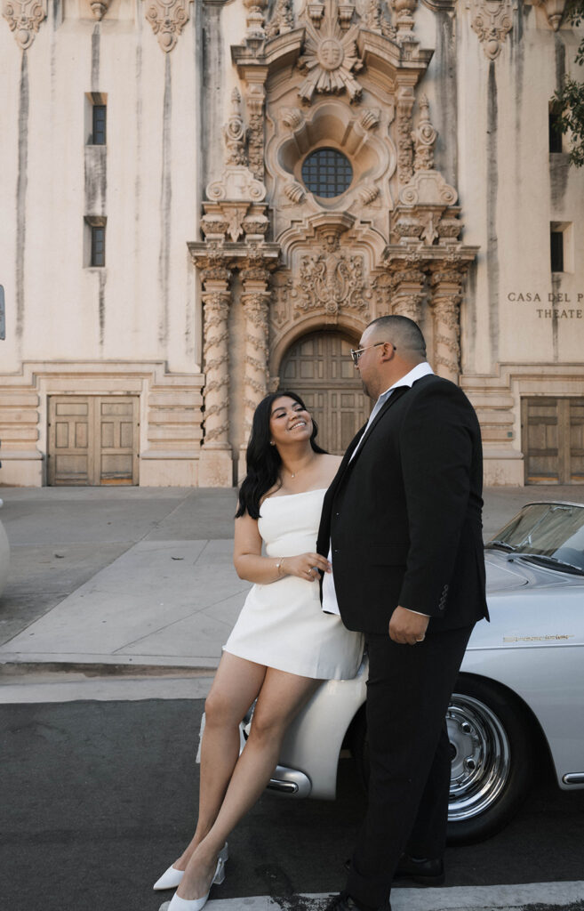 Sabrina and Azor posing in front of a classic vintage car from SD Vintage Rides at Balboa Park, exuding formal glamour.