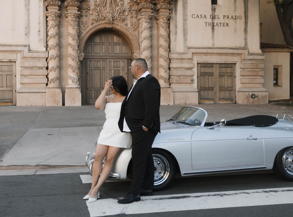 Sabrina and Azor posing in front of a classic vintage car from SD Vintage Rides at Balboa Park, exuding formal glamour.