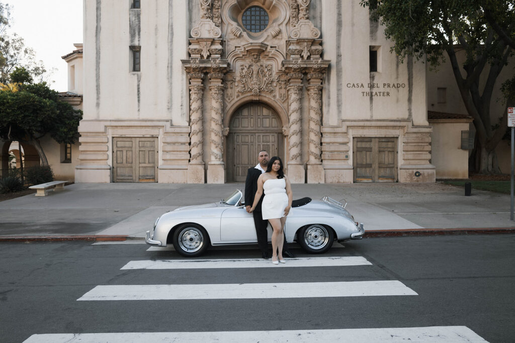 Sabrina and Azor posing in front of a classic vintage car from SD Vintage Rides at Balboa Park, exuding formal glamour.