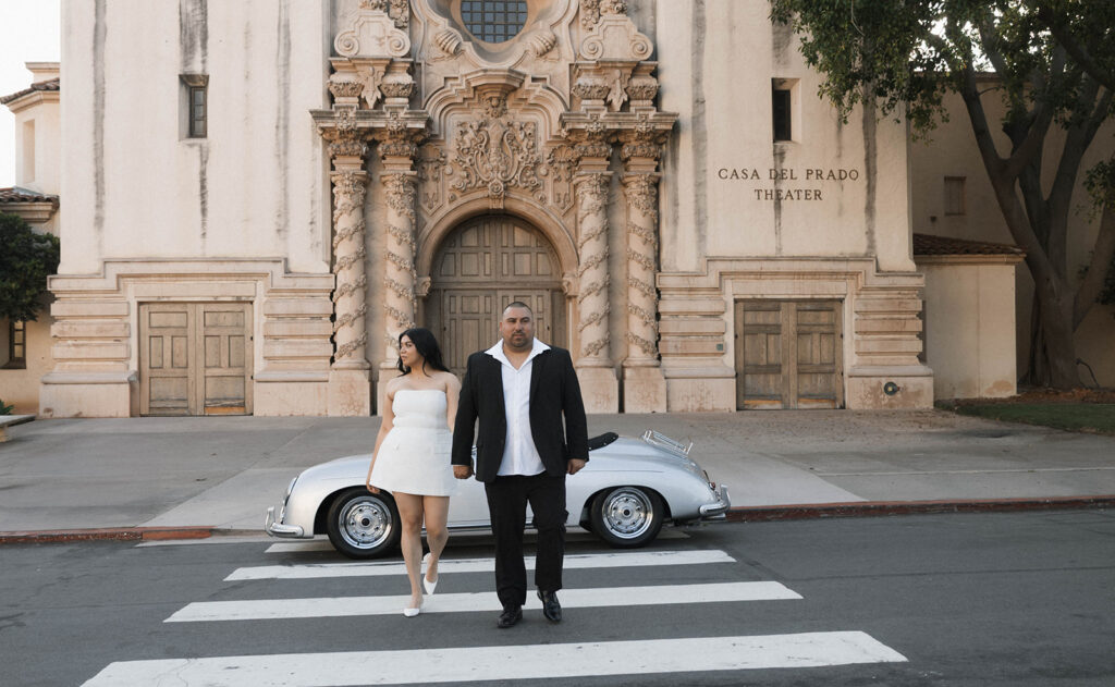 Sabrina and Azor posing in front of a classic vintage car from SD Vintage Rides at Balboa Park, exuding formal glamour.