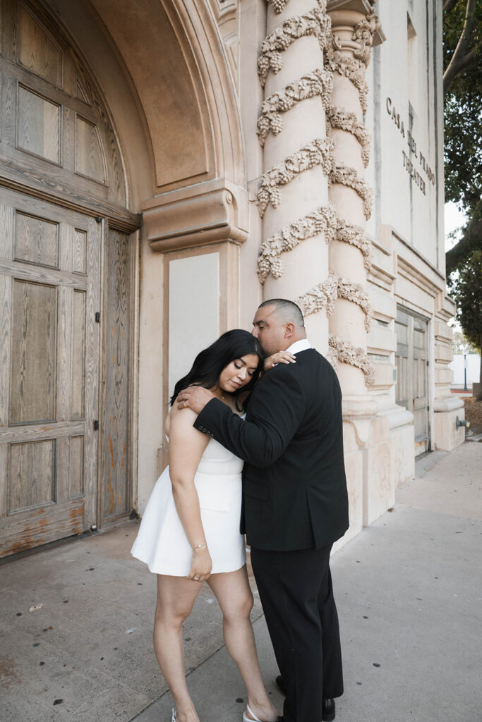 Engaged couple walking hand in hand under the Spanish Colonial arches of Balboa Park, dressed in chic formal attire.
