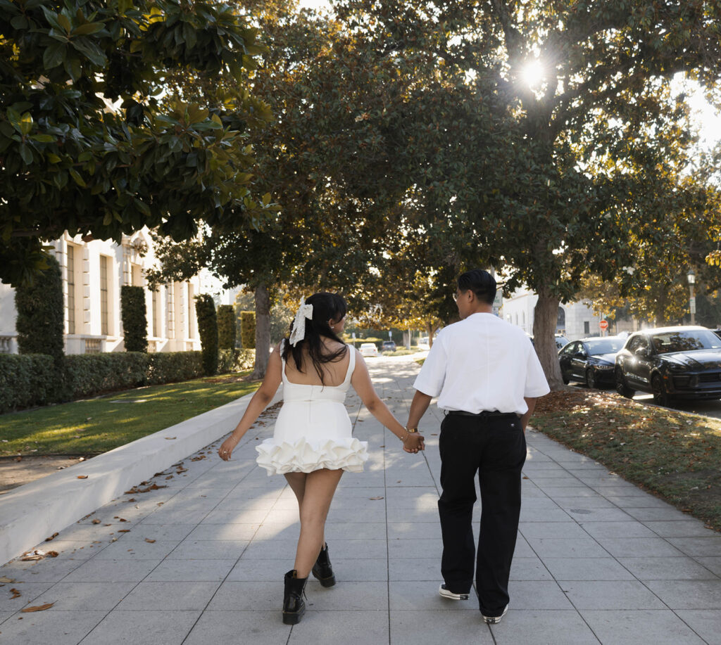 Chris and Andrea share a playful moment dancing on a Pasadena sidewalk during their engagement session, with Andrea in a white ruffle dress and black combat boots.