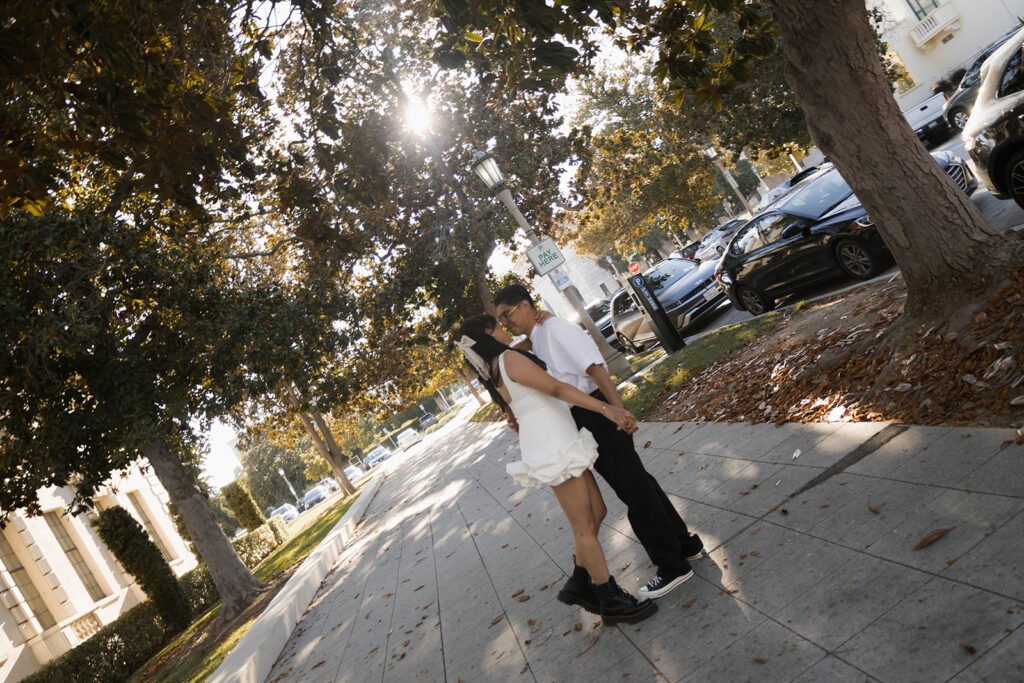 Chris and Andrea share a playful moment dancing on a Pasadena sidewalk during their engagement session, with Andrea in a white ruffle dress and black combat boots.