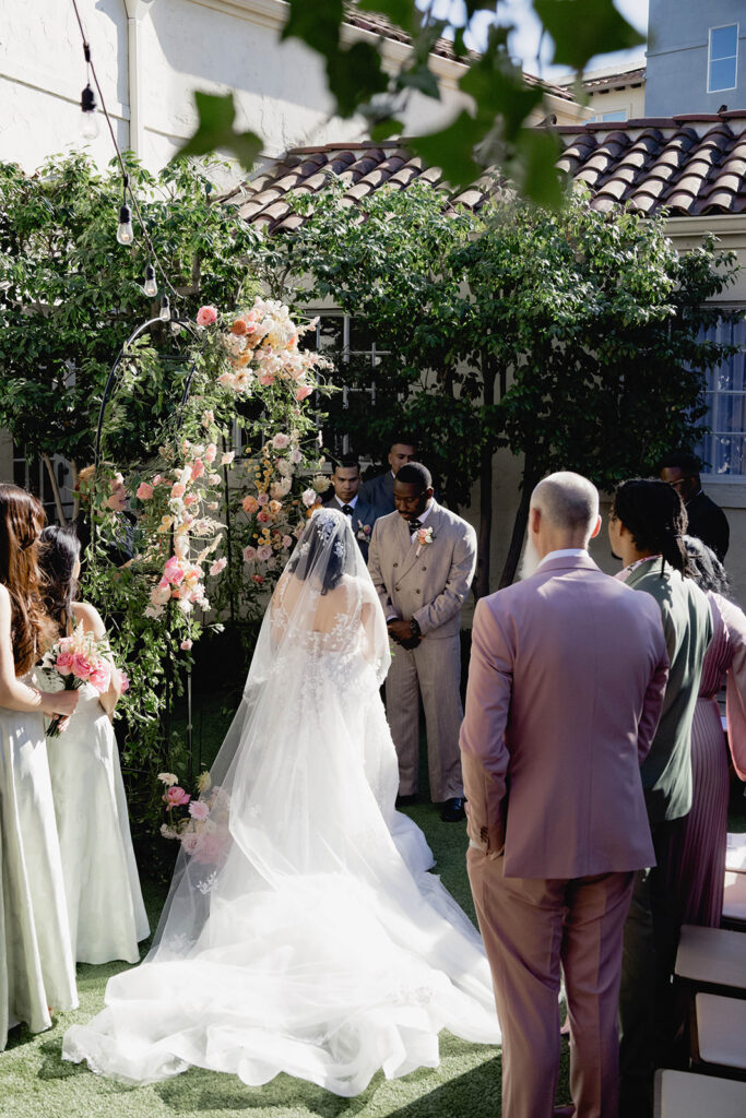 A bride and groom standing together at an alter in a courtyard in formal wedding attire.