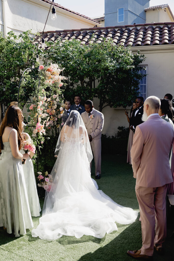 A bride and groom standing together at an alter in a courtyard in formal wedding attire.