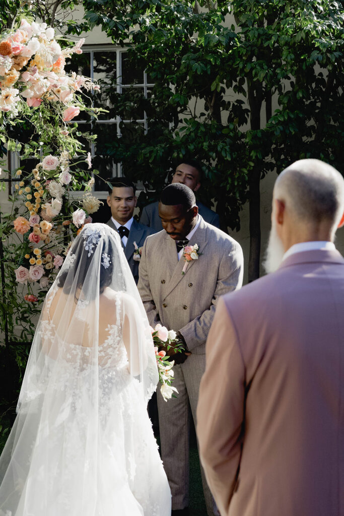 A bride and groom standing together at an alter in a courtyard in formal wedding attire.