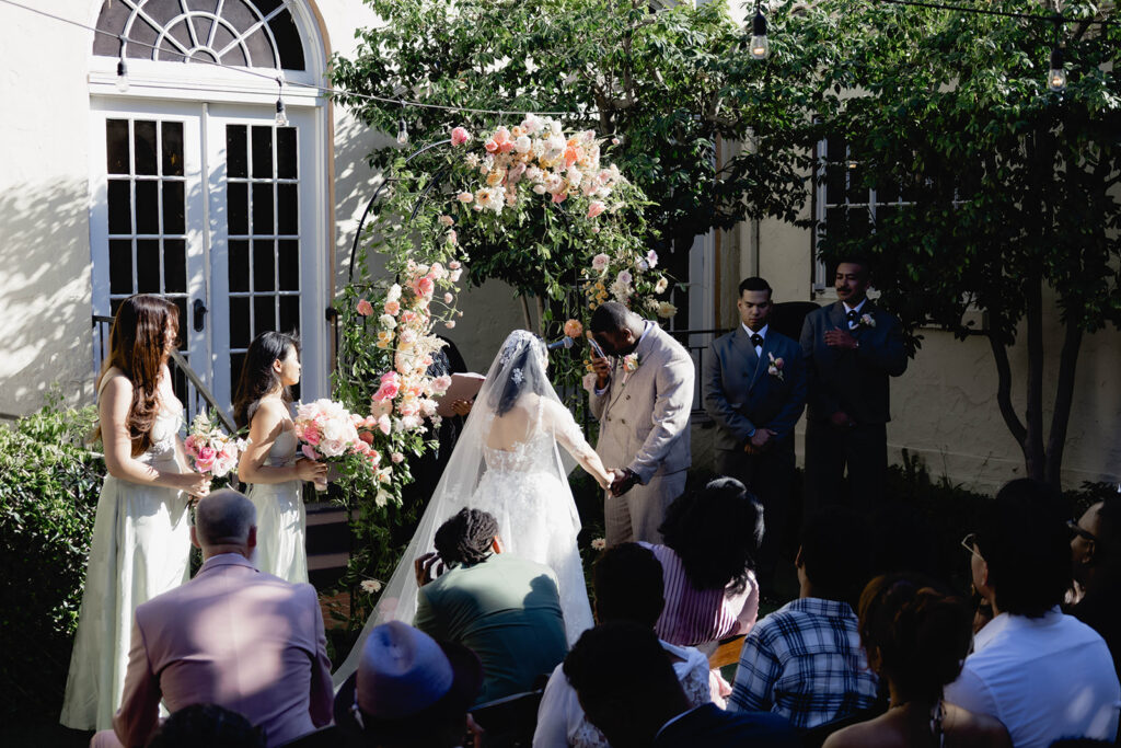 A bride and groom standing together at an alter in a courtyard in formal wedding attire.