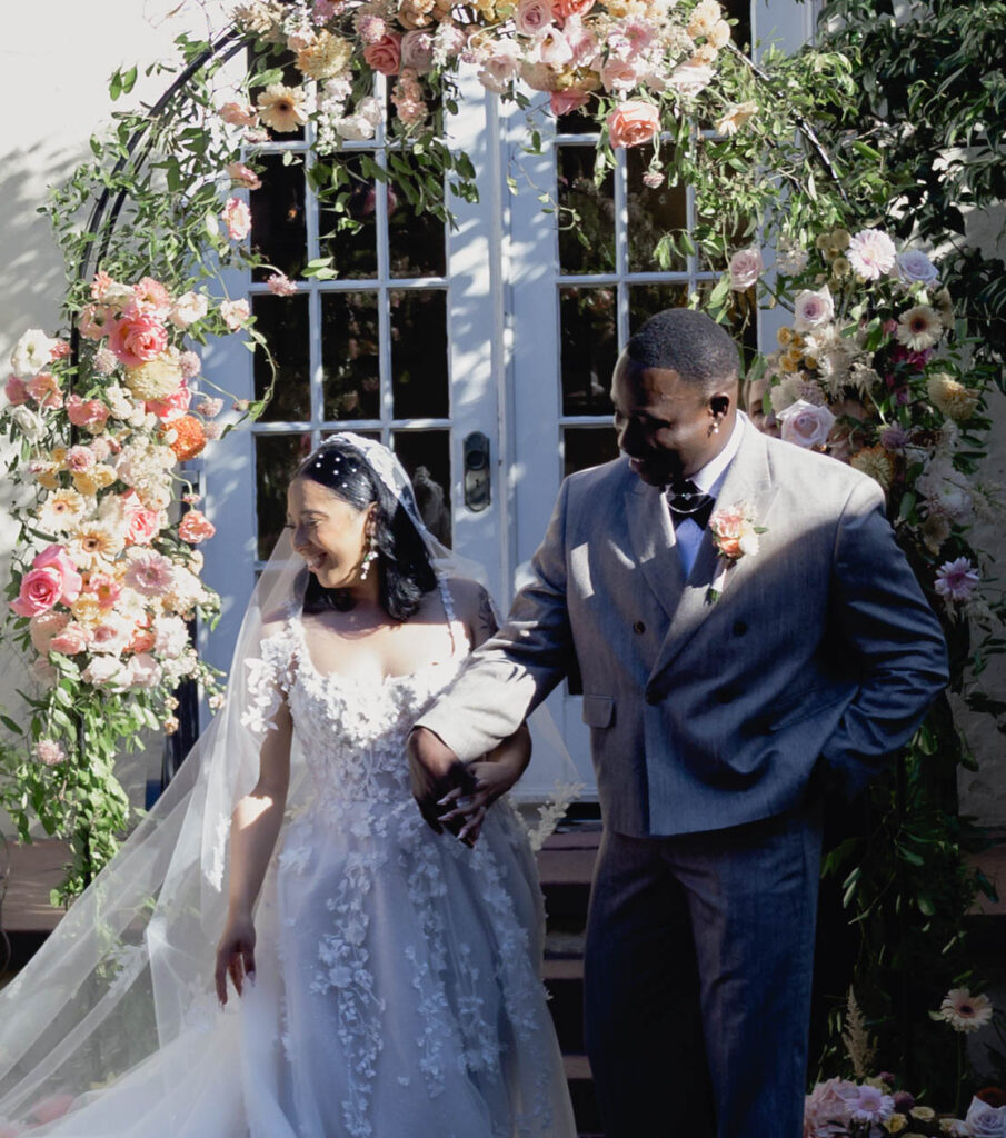 A bride and groom standing together at an alter in a courtyard in formal wedding attire.