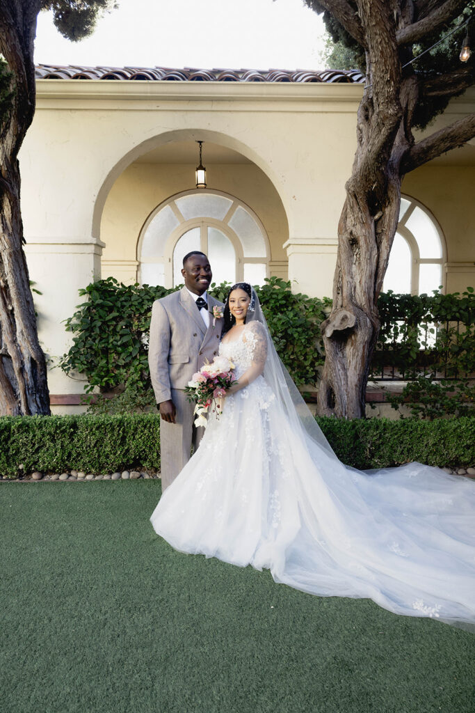 A bride and groom standing together in a courtyard in formal wedding attire.