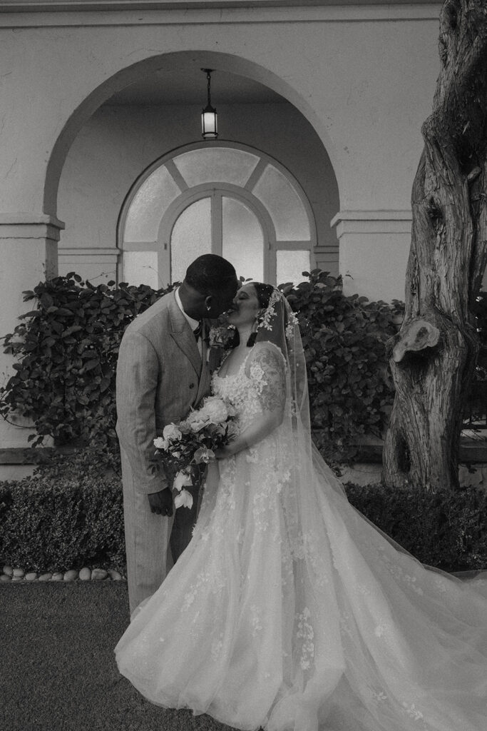 A bride and groom standing together in a courtyard in formal wedding attire.