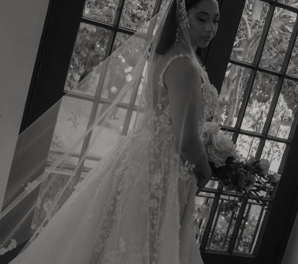 A bride standing indoors in formal wedding attire.