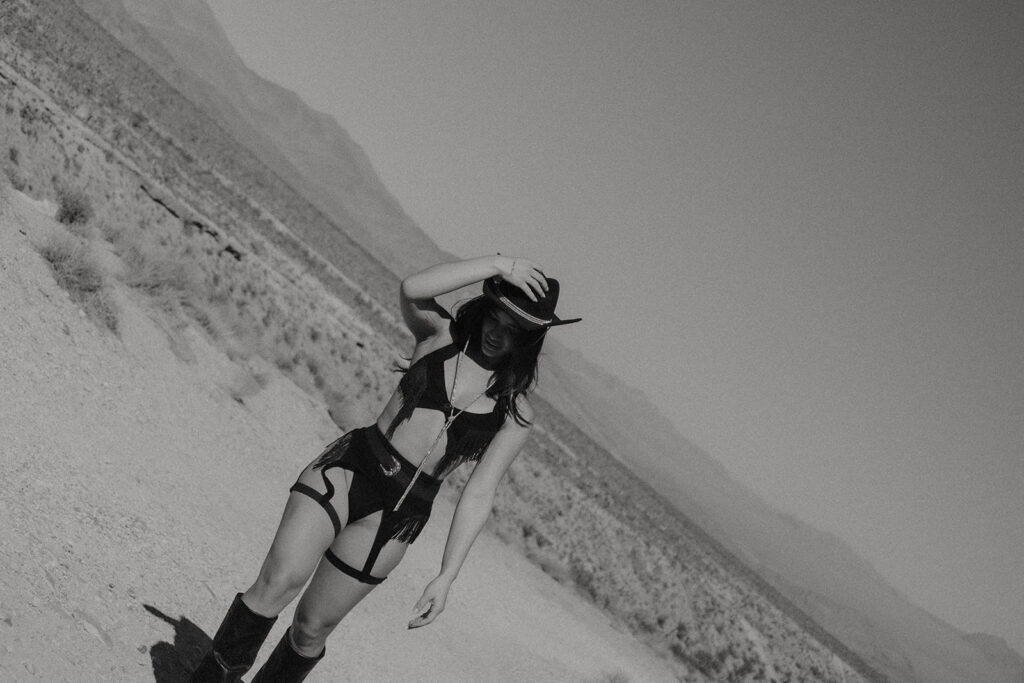 Cowgirl posing in the middle of a Nevada desert road wearing a black cowboy hat and boots during a desert cowgirl photoshoot.