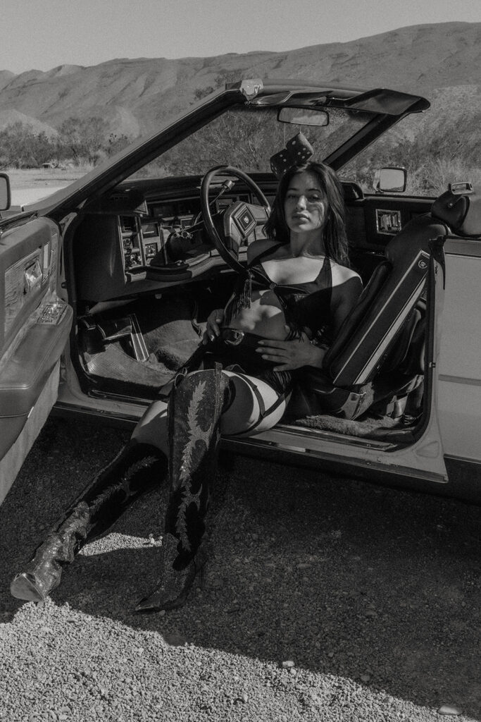 Cowgirl posing in the middle of a Nevada desert road wearing a black cowboy hat and boots during a desert cowgirl photoshoot.