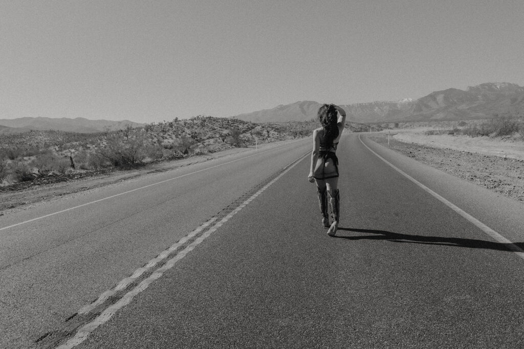 Cowgirl posing in the middle of a Nevada desert road wearing a black cowboy hat and boots during a desert cowgirl photoshoot.