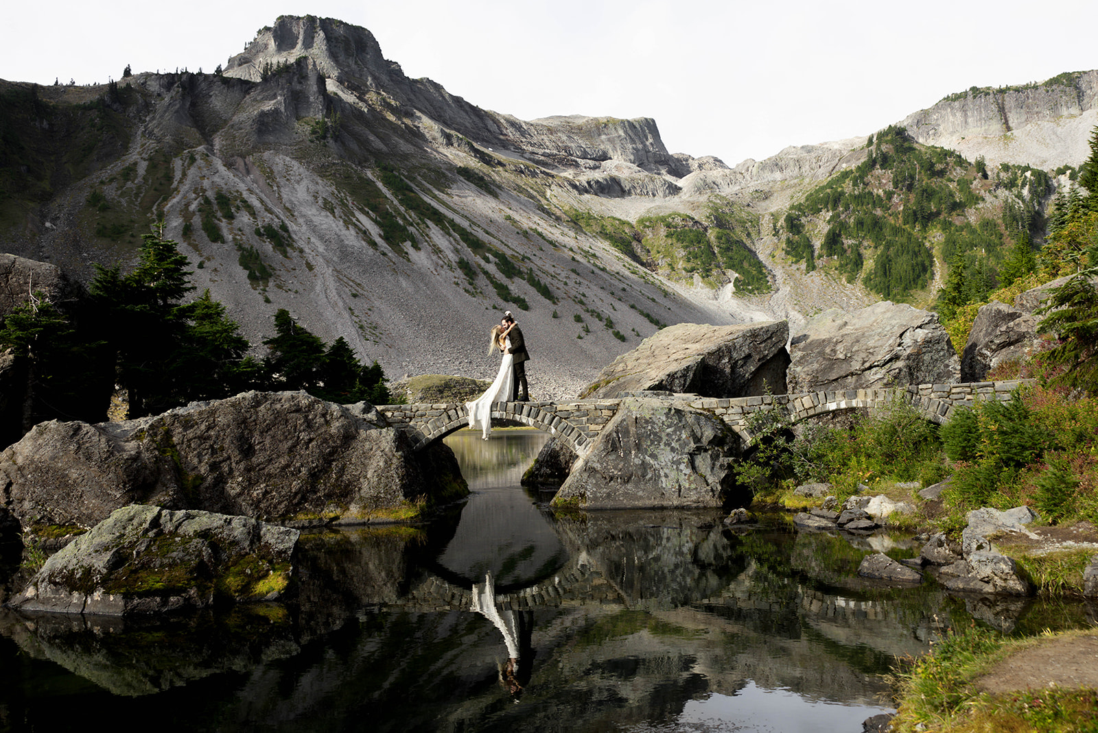 bride and groom embracing on a stone bridge over a lake in the north cascades mountains in washington